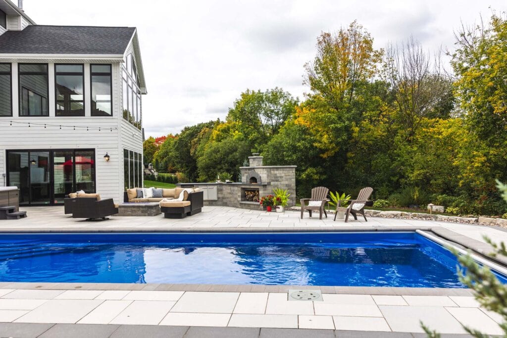 Opened fiberglass pool with clear blue water next to a paver patio and stone pizza oven in Wisconsin