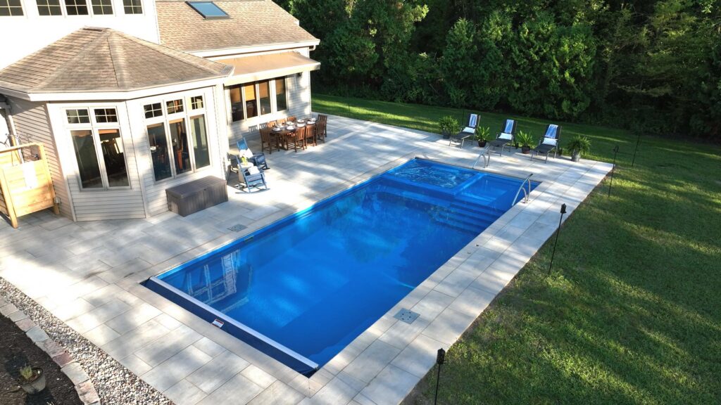 Elevated view of a fiberglass pool and attached spa with paver patio and lounge seating