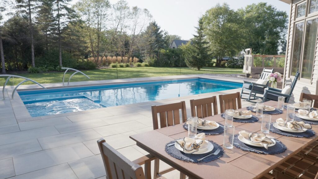 Outdoor dining table set on a paver patio beside a fiberglass pool