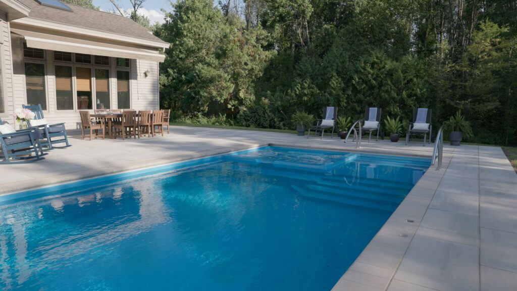 Fiberglass pool with paver deck and lounge chairs along the tree line