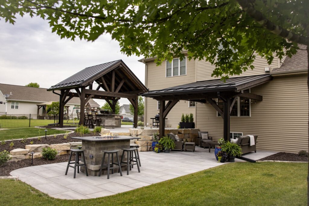 Timber pavilion and attached patio cover over a paver patio with a stone bar and stools