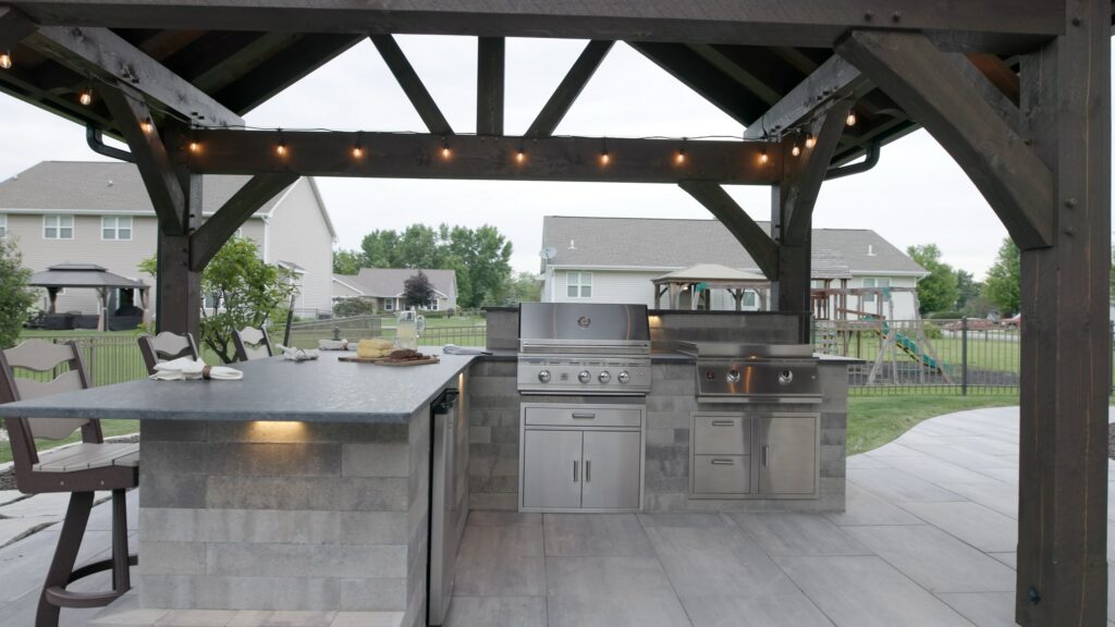 Outdoor kitchen with a built-in grill under a timber pavilion strung with cafe lights