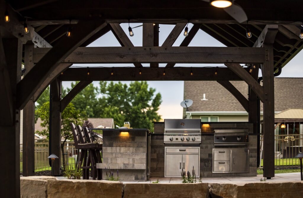 Built-in grill and stone counter under a timber pavilion at dusk