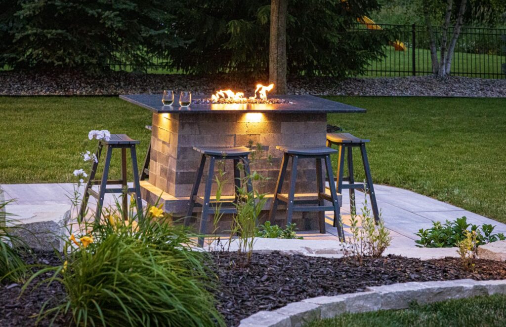 Stone fire table with bar stools on a paver patio at dusk