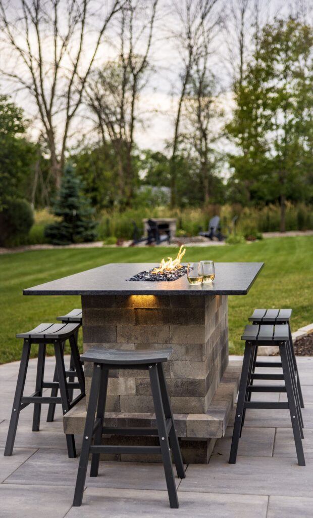 Stone fire table with black bar stools on a paver patio in the evening