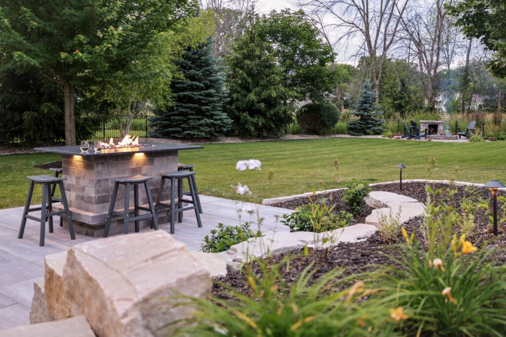 Stone fire table with bar stools on a paver patio overlooking the lawn
