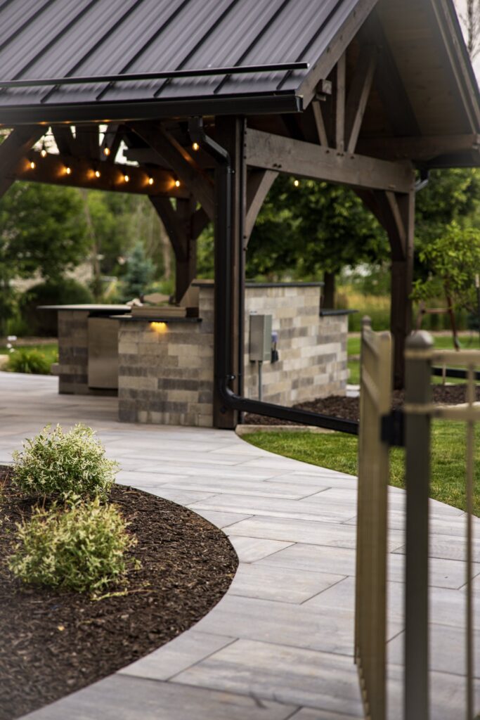 Outdoor kitchen under the timber pavilion beside a curved paver walkway