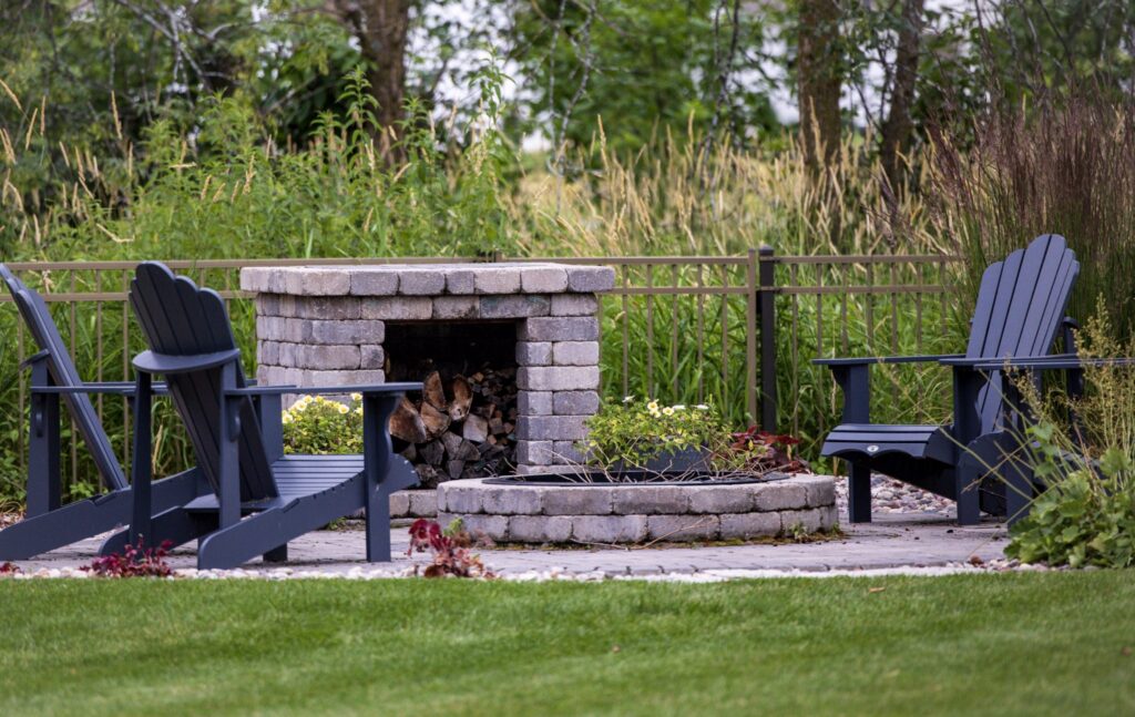 Stone outdoor fireplace with Adirondack chairs and ornamental grasses